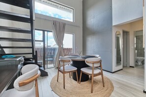 Un intérieur moderne avec une table à manger ronde, quatre chaises, un tapis tissé et une vue sur l’extérieur grâce à de grandes fenêtres.