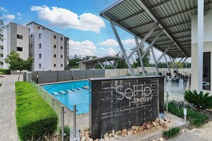 A modern building with a swimming pool, a covered outdoor area, and a sign that reads 'SOHO Junction'. - Soho Junction Stylish 2-Bed Loft by ctha (Sandton)