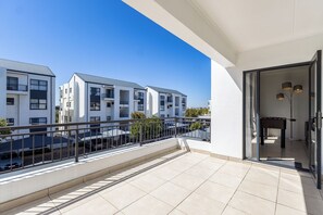 A modern apartment with a balcony, a dining area, and a view of neighboring buildings. - The Sandown Escape, Pool and Gym by ctha (Cape Town)