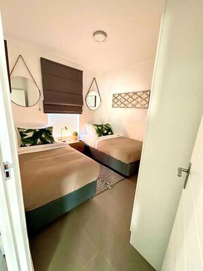 A bedroom with two beds, a bedside table, a lamp, and a wall-mounted mirror. - Wonderful 2-bedroom apartment in welcoming Bloubergstrand neighborhood (Cape Town)