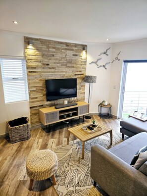 Ein modernes Wohnzimmer mit Flachbildfernseher, Holzboden, einer Couch, einem Couchtisch und einer an der Wand montierten TV-Konsole.