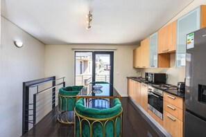 A modern kitchen with a dining area, stainless steel appliances, and a view through the glass door. - Chic Queens Gate Duplex by Ctha (Cape Town)