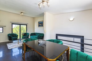 A modern living room with a glass-top table, green sofas, and a balcony railing. - Chic Queens Gate Duplex by Ctha (Cape Town)
