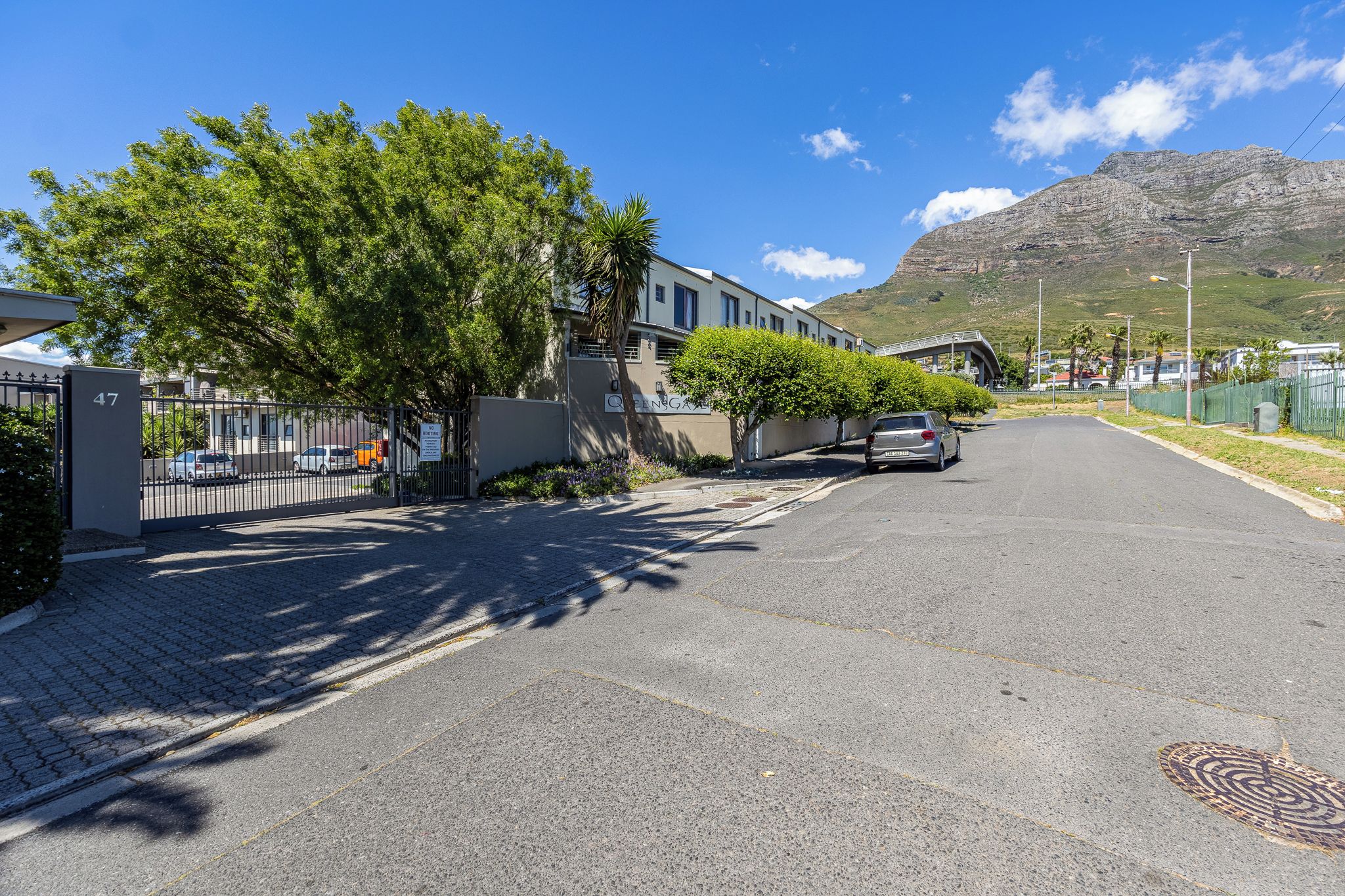 A residential street with houses, a gated entrance, and a mountain in the background.