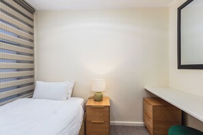 Ein Hotelzimmer mit Bett, Nachttisch mit Lampe, Schreibtisch und Spiegel.