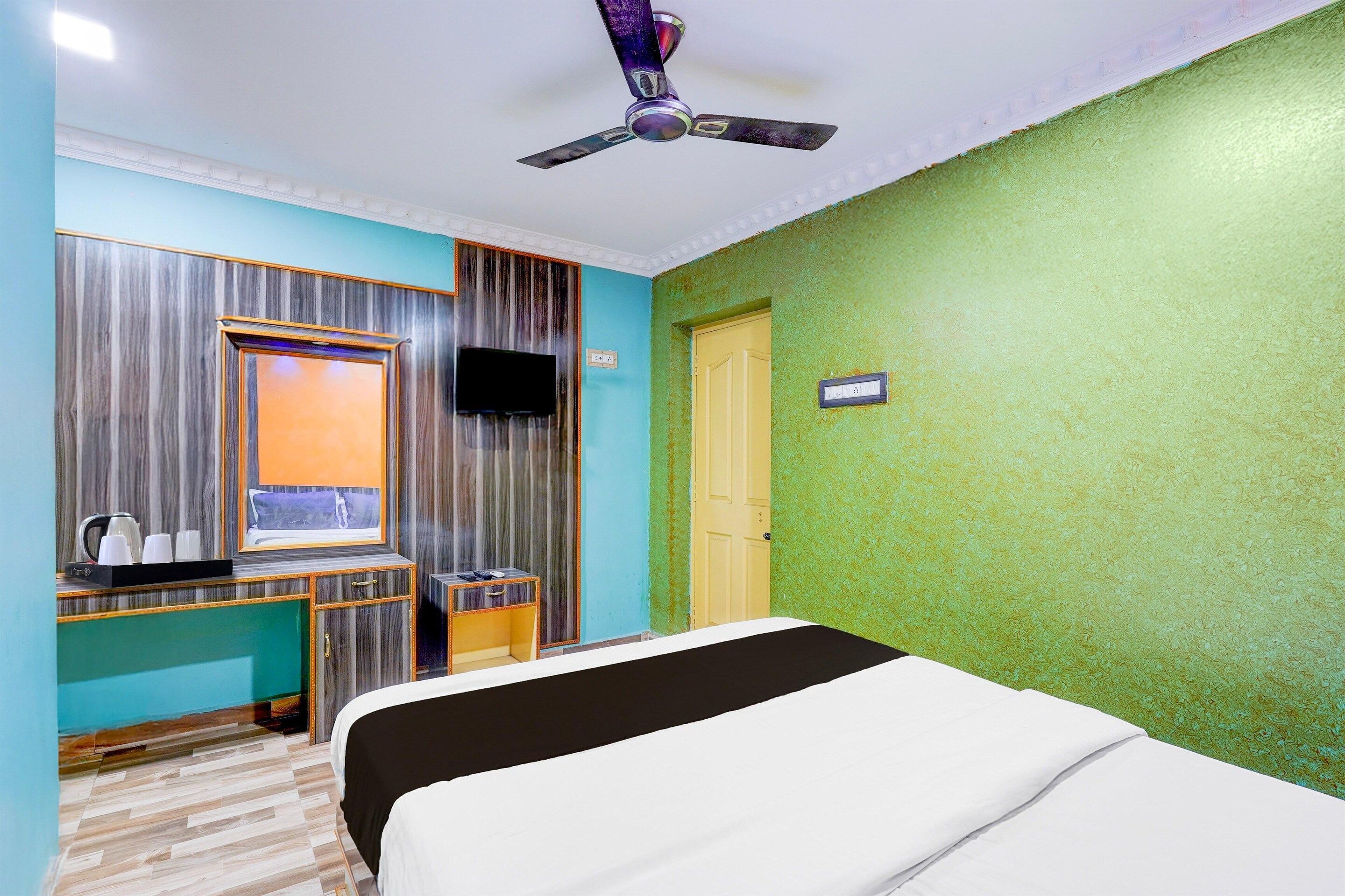 A hotel room with a bed, a desk with a mirror, a television, and a ceiling fan.