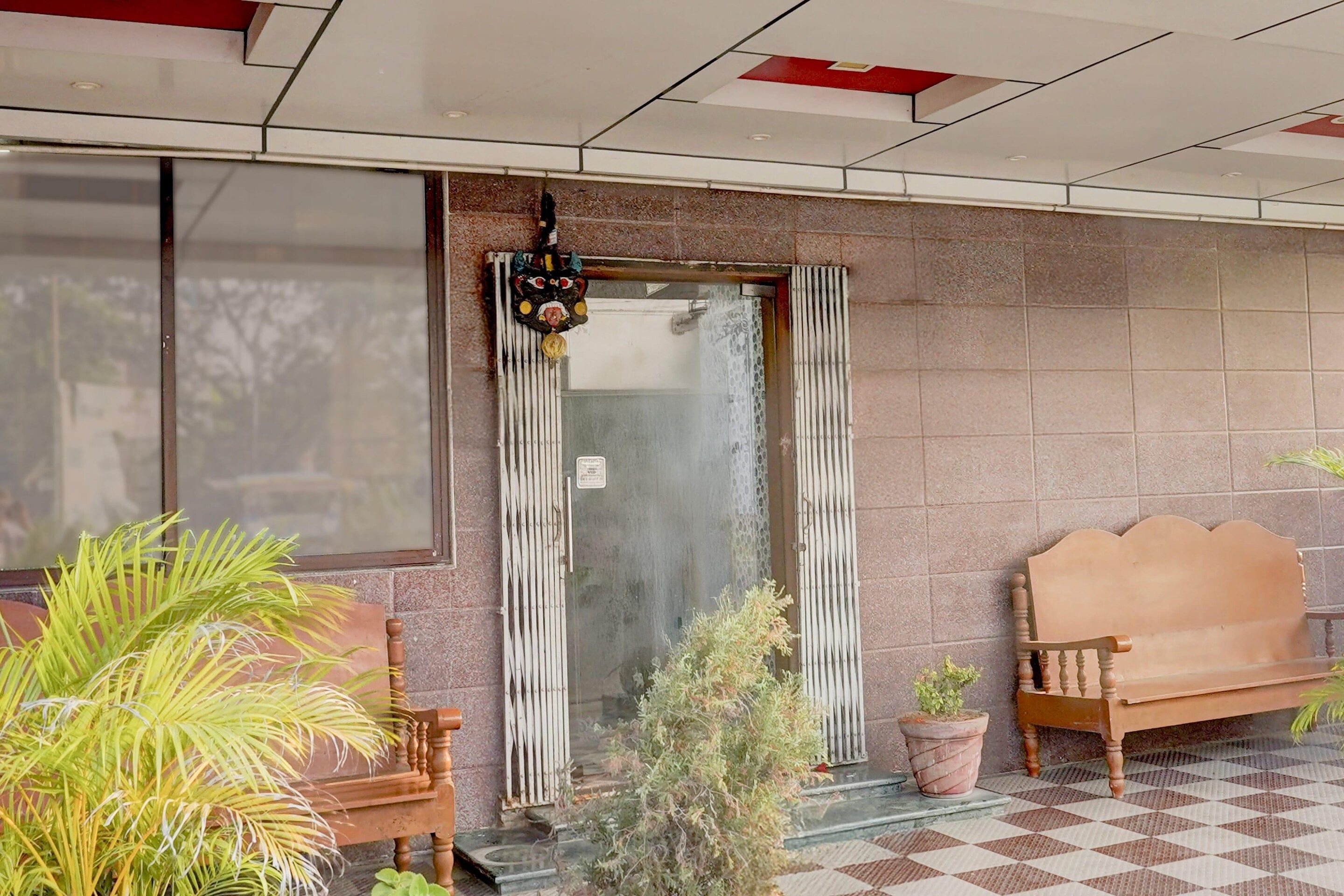 Entrada de hotel con piso a cuadros, un banco de madera y plantas en macetas.