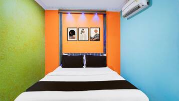 A hotel room with a bed, a wall-mounted air conditioner, and three framed artworks above the bed.