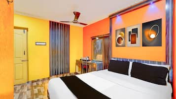 A hotel room with a bed, a desk, a chair, a ceiling fan, and artwork on the wall.