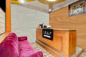 Un área de recepción con un mostrador de madera, un sofá rosa acolchado y un papel tapiz estampado.