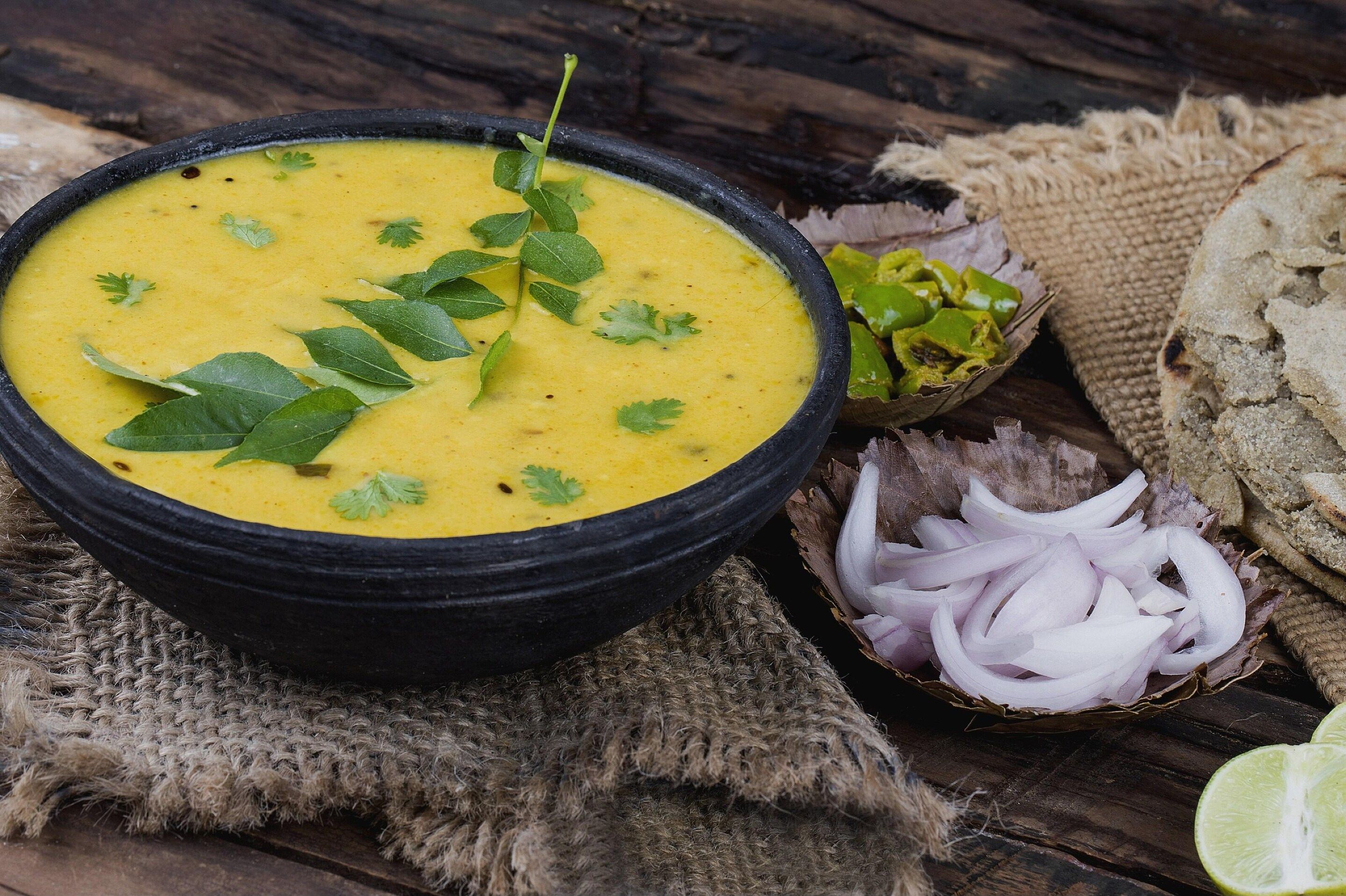 A bowl of dal with cilantro garnish, accompanied by sliced onions and a lime half on a rustic wooden surface.
