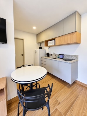 A compact kitchen with a white refrigerator, a microwave on a wooden shelf, a coffee maker, and a sink with a granite countertop. - New Listing (São Paulo)