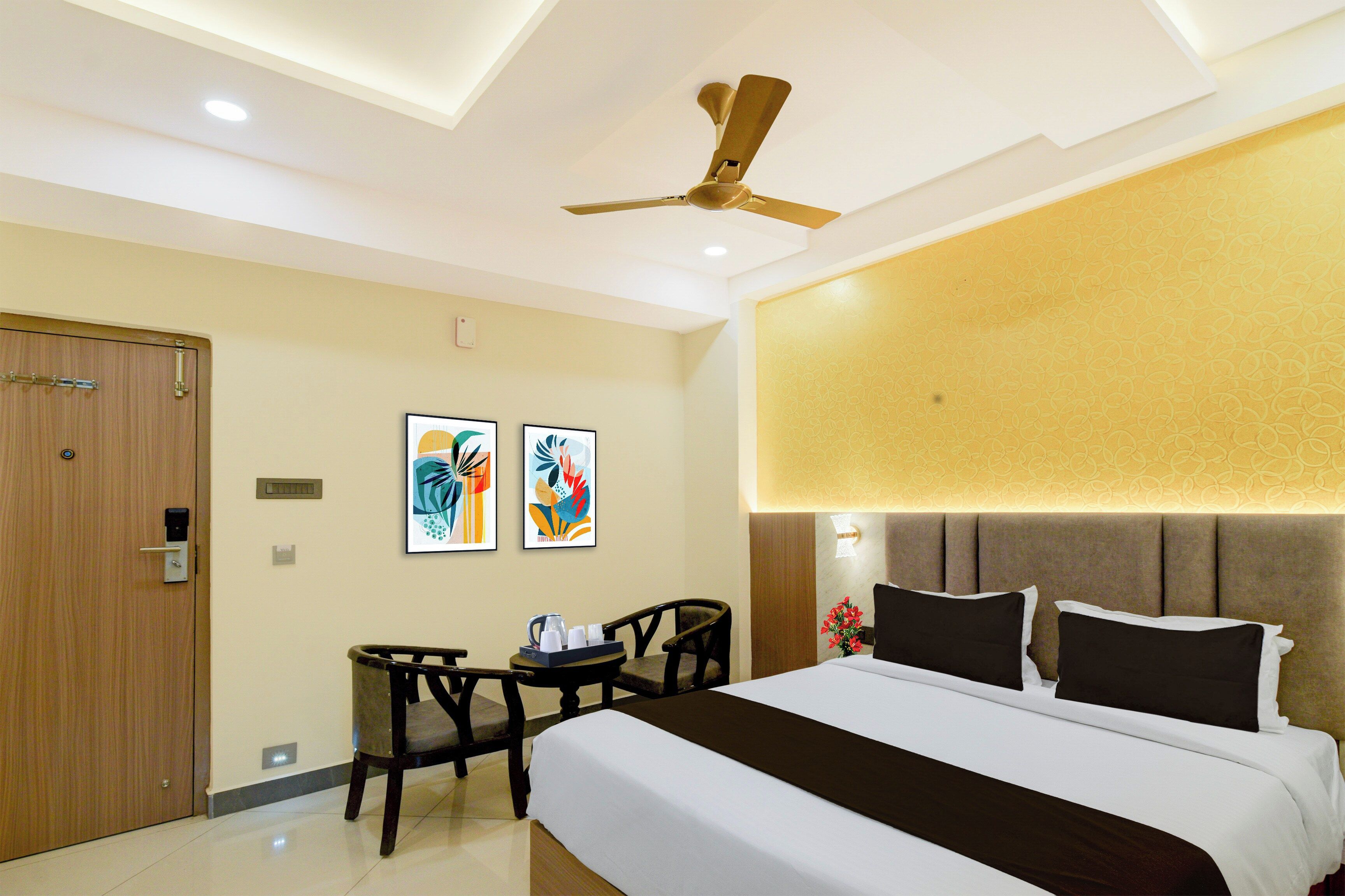 Une chambre d’hôtel avec un lit, un bureau et une chaise, un ventilateur de plafond et des œuvres d’art accrochées au mur.