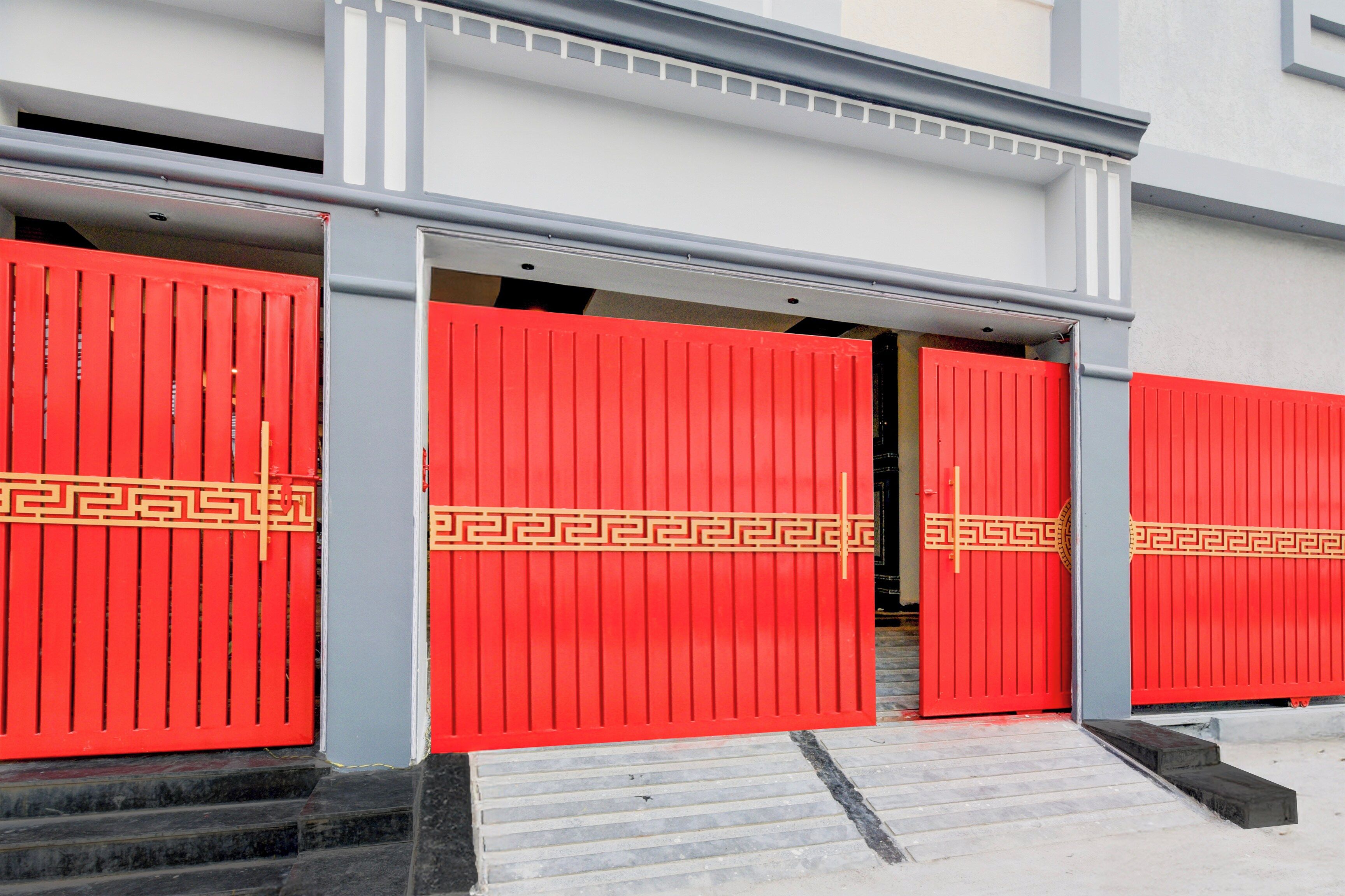 Une entrée d’immeuble avec trois portes rouges ornées d’un motif géométrique.