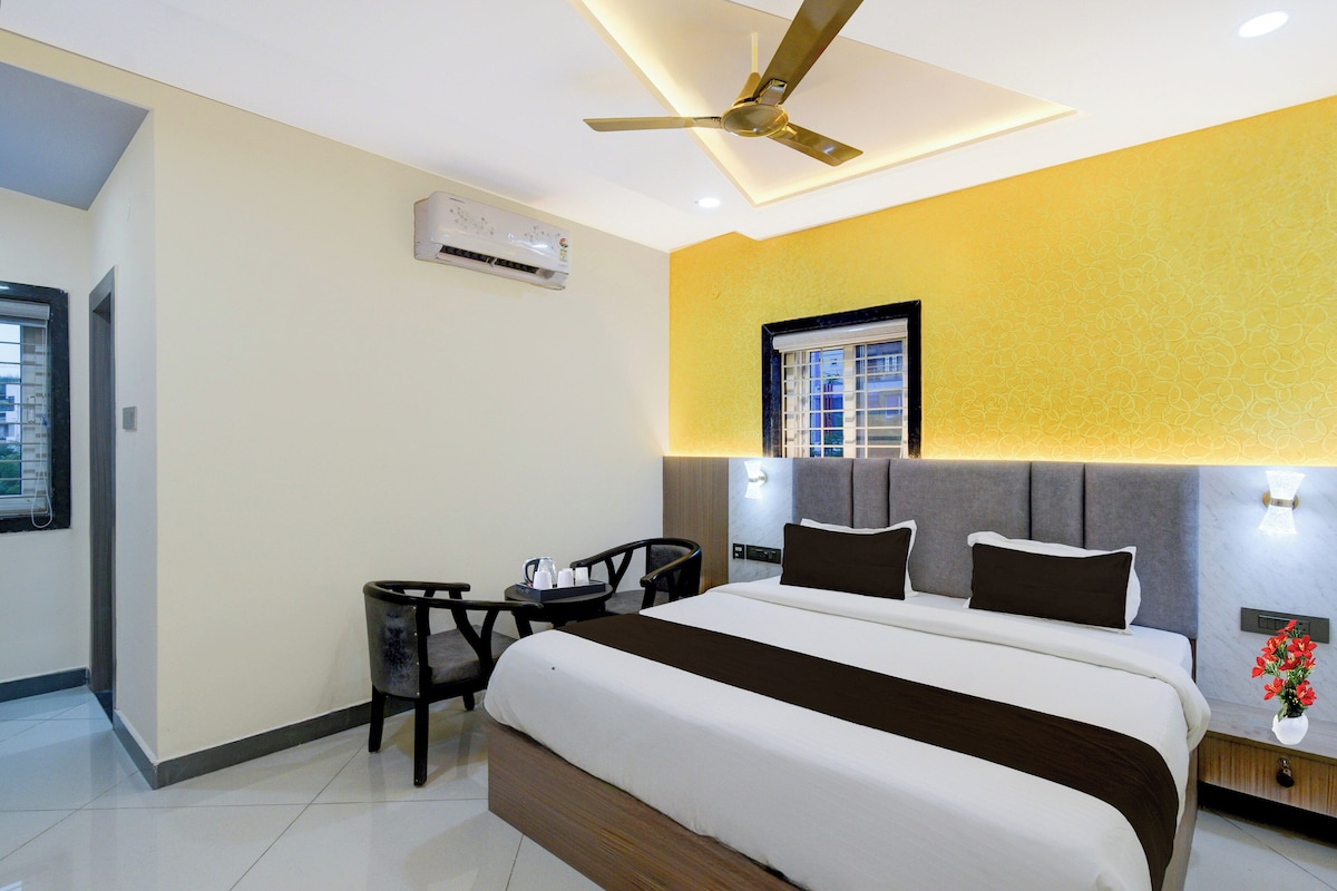 A hotel room with a bed, a desk, a chair, a window, and an air conditioning unit.