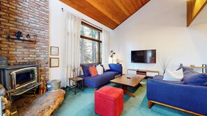 Ein gemütliches Wohnzimmer mit Kamin aus Ziegelsteinen, blauen Sofas, einem Holztisch und einem flachbildfernseher an der Wand.