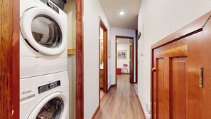 A laundry room with a Whirlpool washer and dryer, wooden flooring, and a hallway leading to a room with a painting. - Spacious Mountain Retreat Near Eagle Lodge, Private Laundry, Fireplace (Mammoth Lakes)
