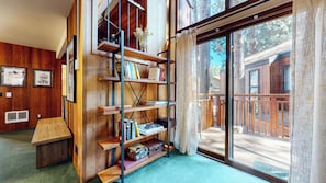 A room with a wooden bookshelf, a small table, and a large sliding glass door leading to an outdoor deck. - Spacious Mountain Retreat Near Eagle Lodge, Private Laundry, Fireplace (Mammoth Lakes)