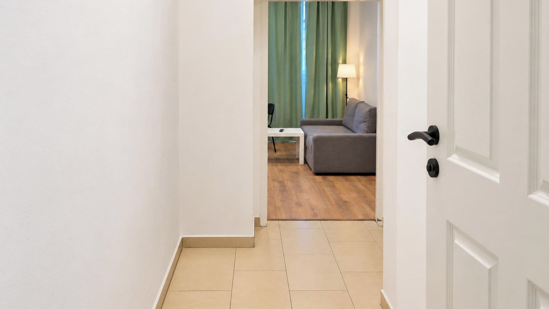 A hallway leading to a living area with a sofa, a small table, and a lamp.