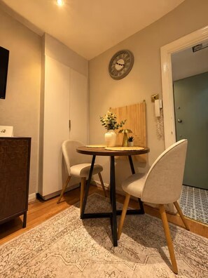 A dining area with a round table, two chairs, a clock on the wall, and a door in the background. - Kings Cross 1-bed Apt, Sleeps 3 With Great Views (London)