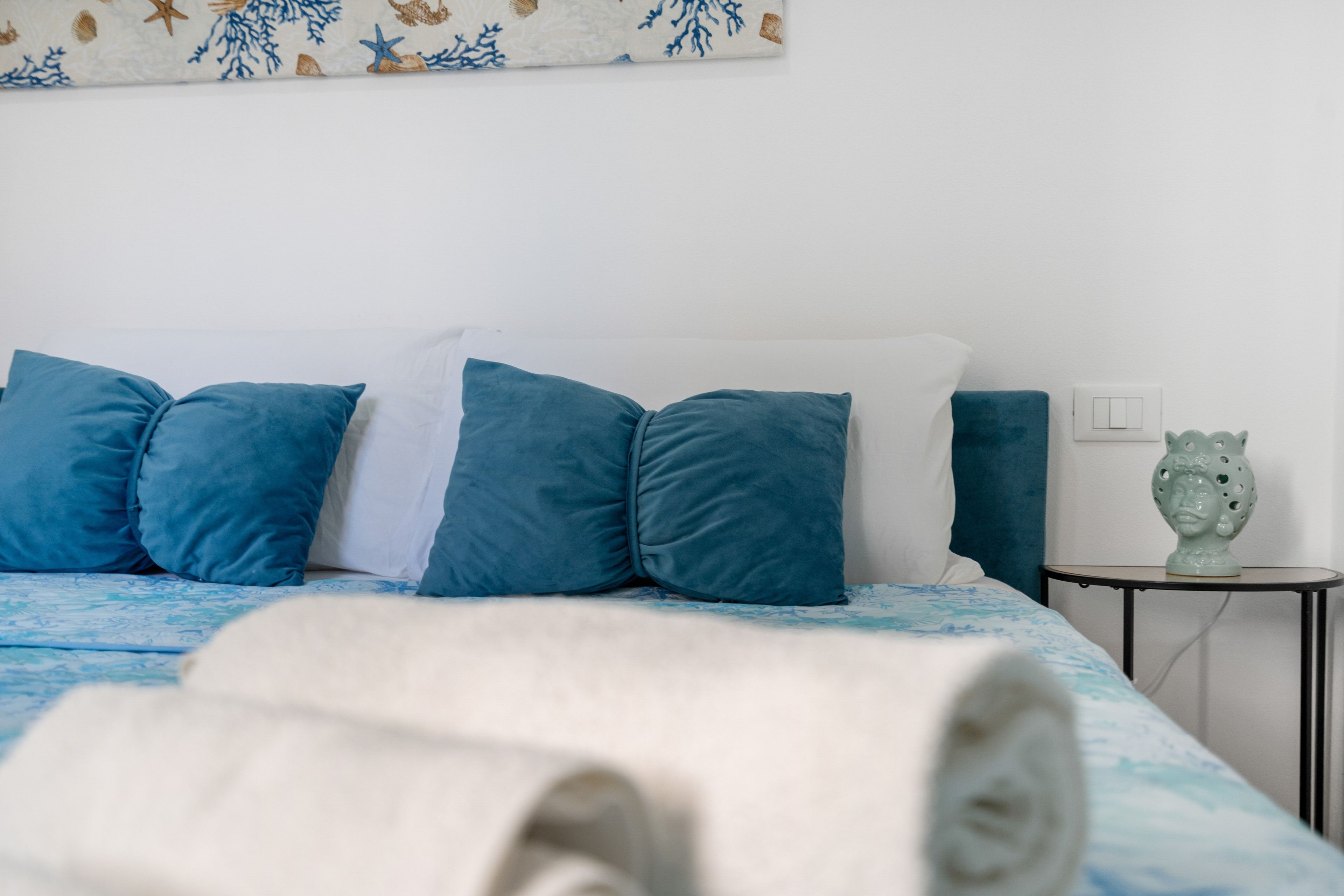 Un letto rifatto con cuscini blu e bianchi, una coperta bianca e una scultura decorativa su un comodino.
