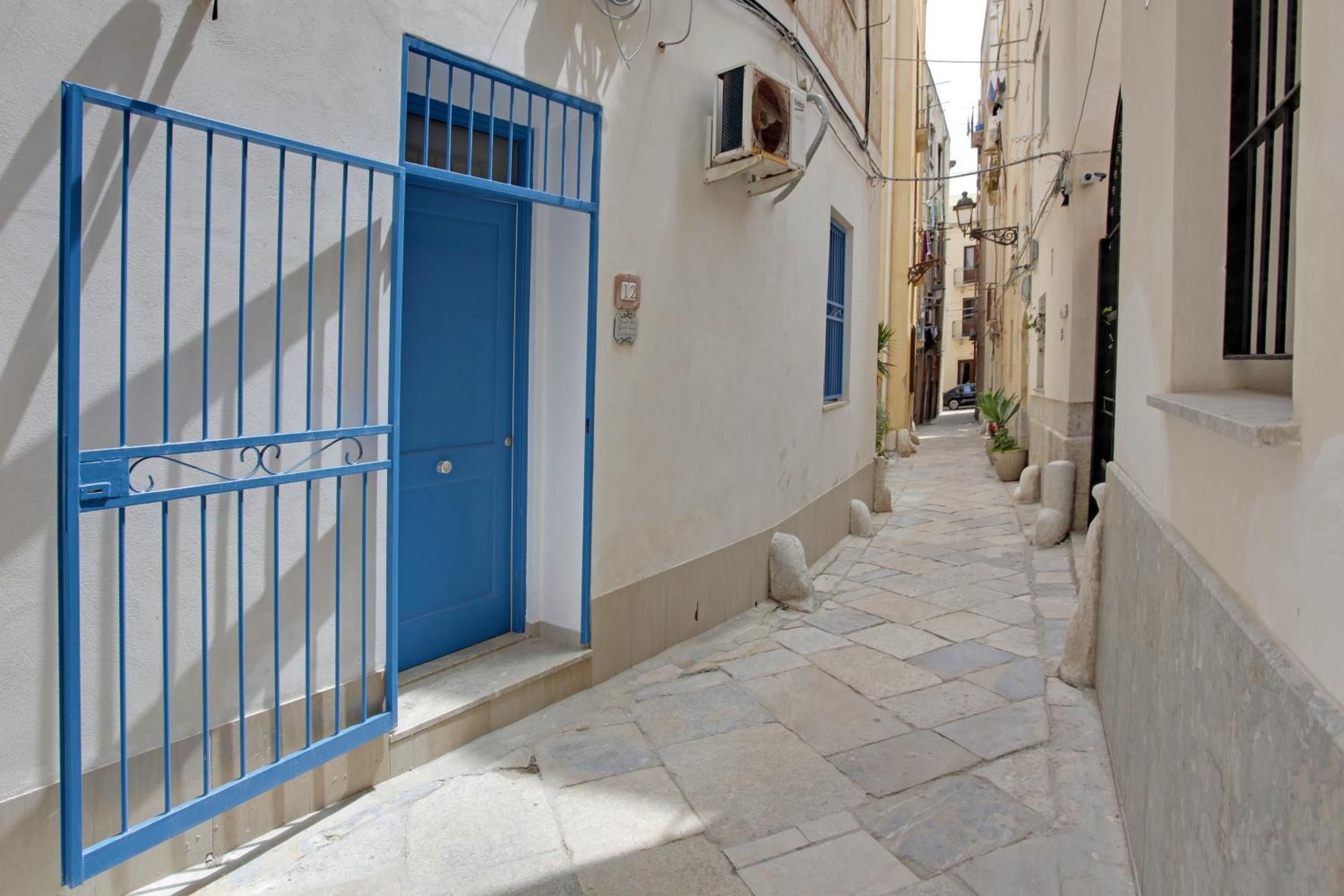 Un stretto vicolo con un cancello blu e un edificio bianco.