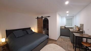 Una camera compatta con un letto, un comodino e un angolo cottura piccolo.