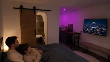 Een slaapkamer met een bed, een aan de muur bevestigde televisie en een bureau met stoel.