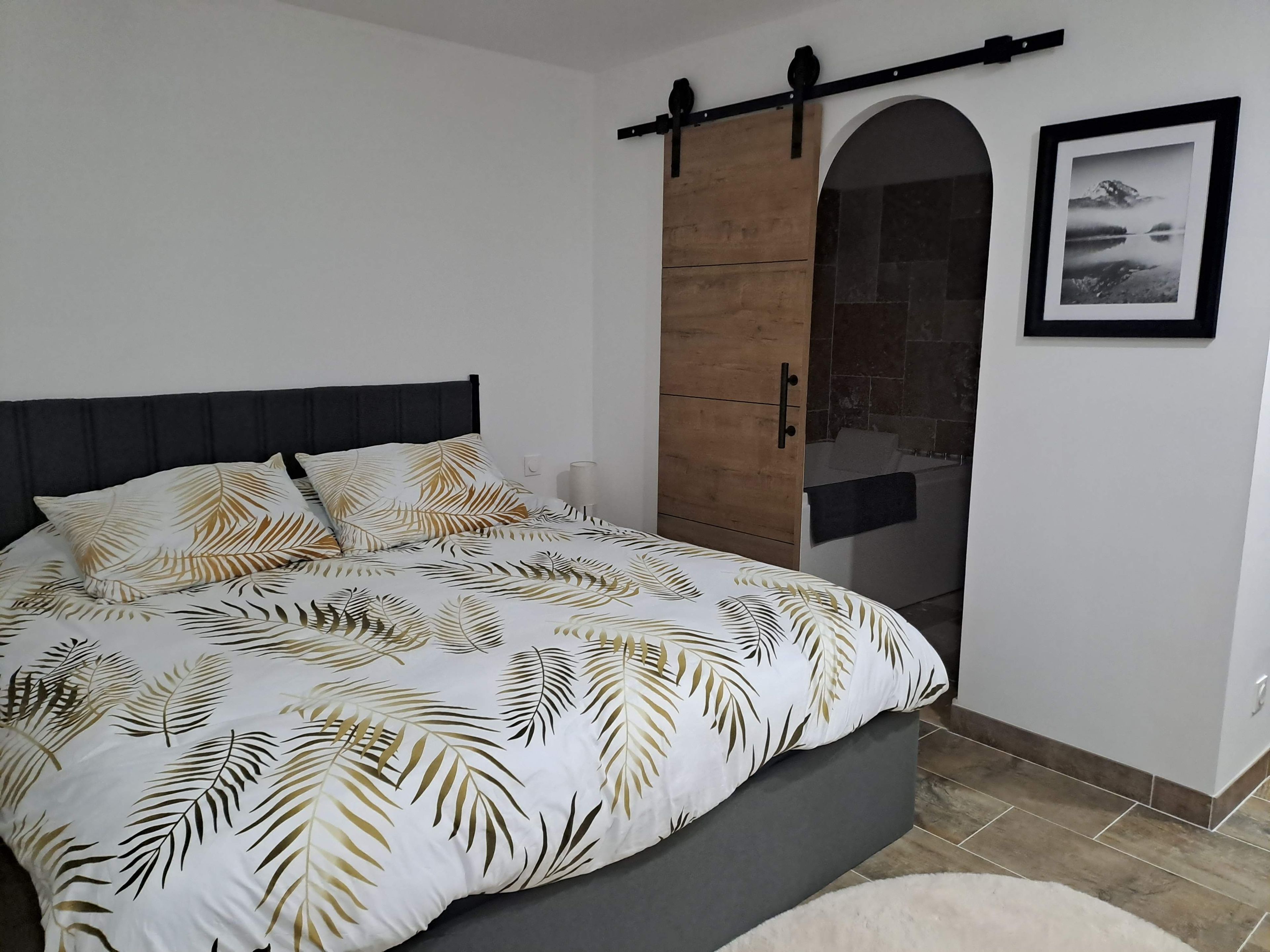 Een slaapkamer met een bed, een houten garderobe, een badkamer met een bad en een inlijsting foto aan de muur.