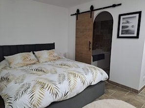 Un dormitorio con cama, un armario de madera, un baño con bañera y un cuadro en la pared.