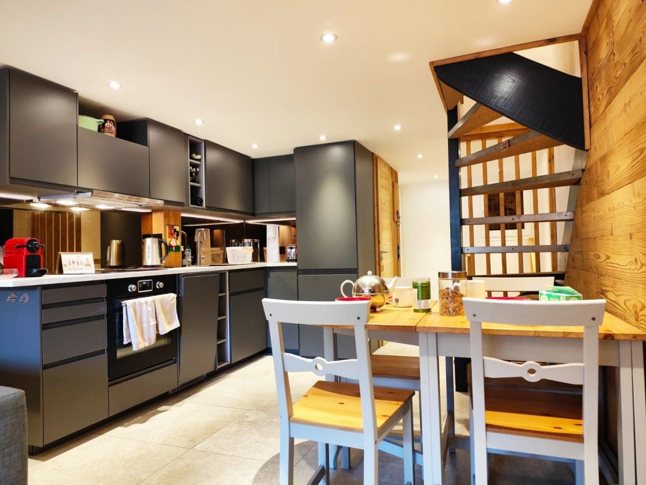 Una cocina moderna con armarios oscuros, una mesa de comedor de madera y una silla blanca.