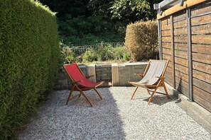 Two wooden lounge chairs with canvas seats, positioned on a gravel patio adjacent to a stone wall and a wooden fence. - La Kabane d'Orsin (4 people) Close to the ski slopes & free parking (Saint-Gervais-les-Bains)