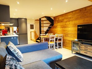 A modern living room with a grey sofa, a wooden accent wall, a TV, and a staircase leading to another level. - La Kabane d'Orsin (4 people) Close to the ski slopes & free parking (Saint-Gervais-les-Bains)