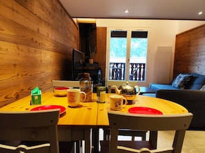 A dining area with a wooden table and chairs, a coffee machine, and a view of the outdoors through a glass door. - La Kabane d'Orsin (4 people) Close to the ski slopes & free parking (Saint-Gervais-les-Bains)