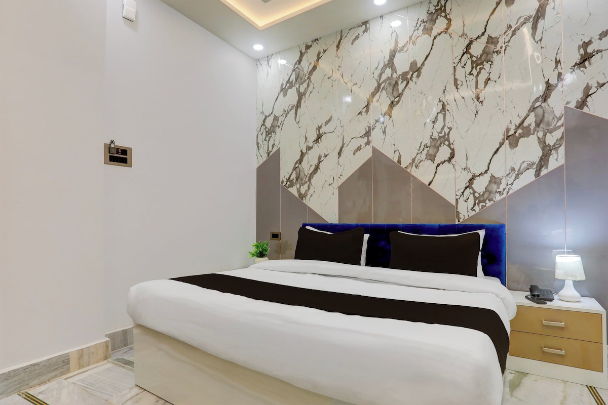 A modern bedroom with a large bed, a nightstand, a lamp, and a wall-mounted heater.