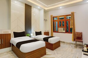 A hotel room with two beds, a wooden wardrobe, a window with curtains, and a small table with a lamp. - Townhouse Vishwanath Temple Varanasi (Varanasi)