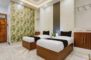 A hotel room with a geometric patterned wall, a large bed with a wooden headboard, a small bedside table, and a wardrobe with a mirror. - Townhouse Vishwanath Temple Varanasi (Varanasi)