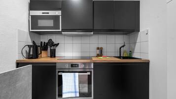 Une cuisine moderne avec des meubles de couleur noire, un plan de travail en bois, un four encastré et un four à micro-ondes.
