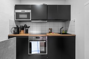 Una cuina moderna amb armaris negres, taulell de fusta, forn integrat i microones.