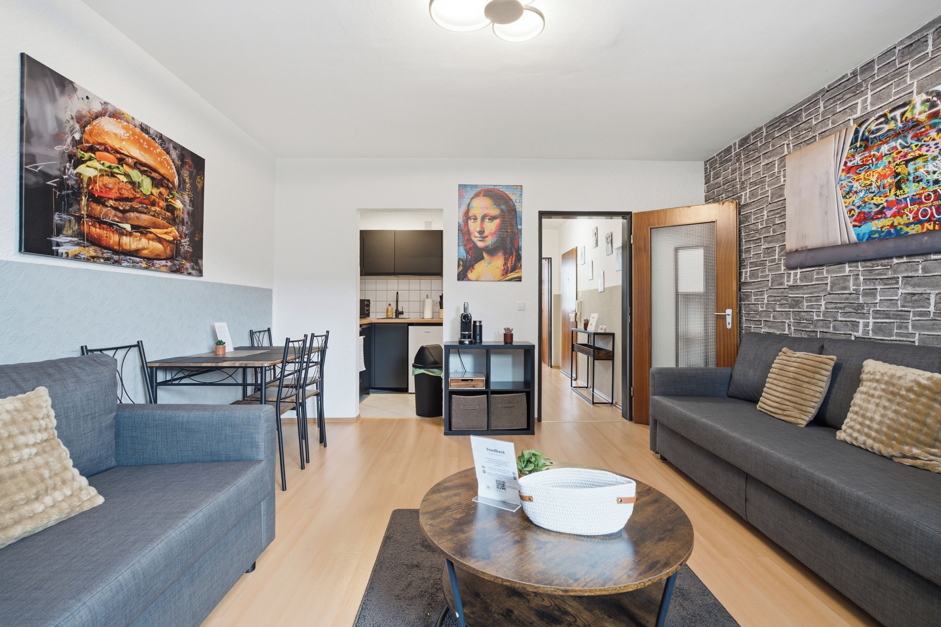 Ein modernes Wohnzimmer mit Essbereich, einer Küche im Hintergrund und Kunstwerken an den Wänden.
