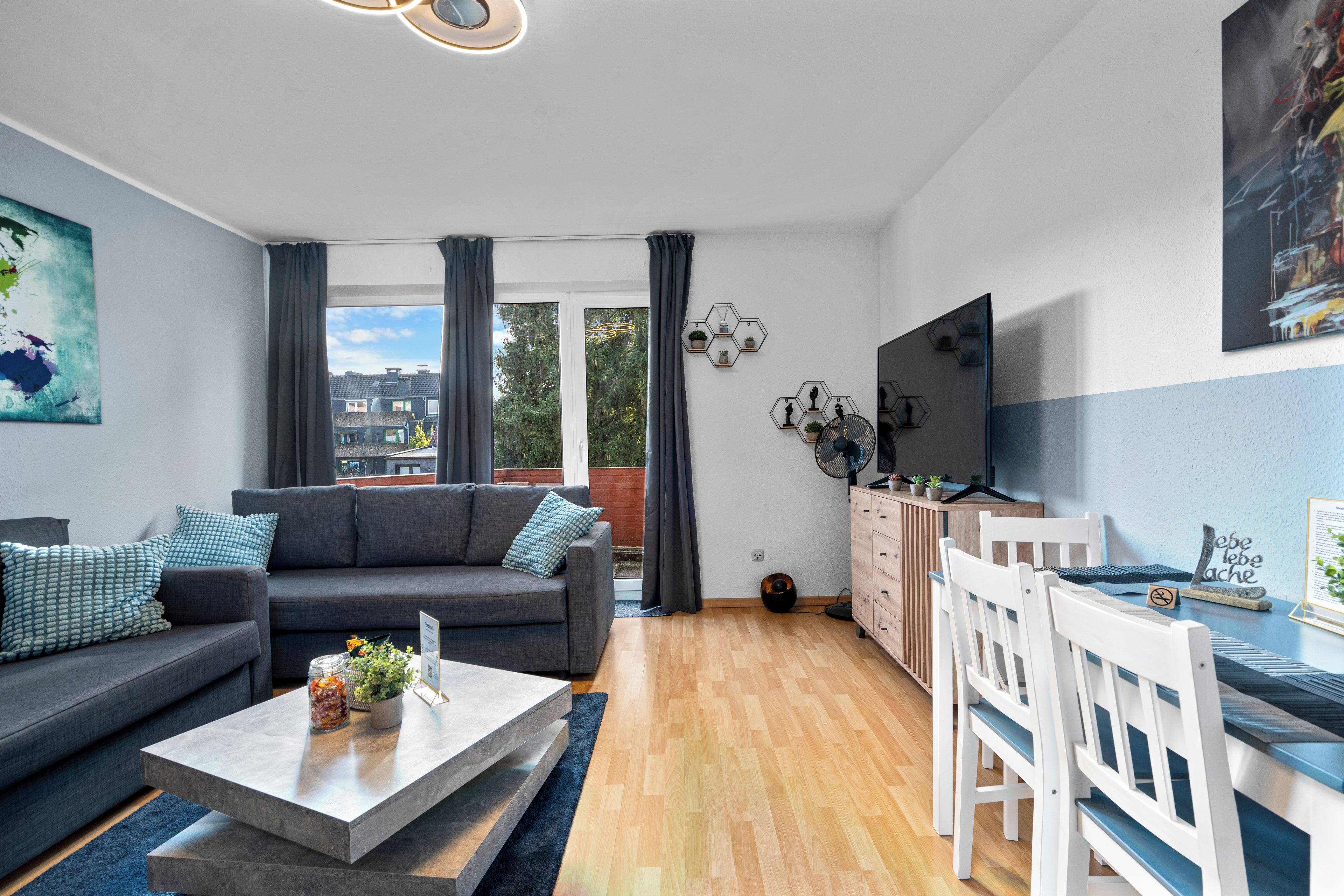A modern living room with a grey sofa, a coffee table, and a dining area with white chairs.