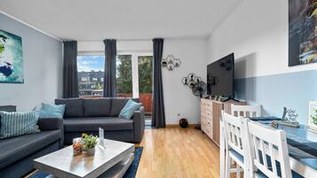 A modern living room with a grey sofa, a coffee table, and a dining area with white chairs.