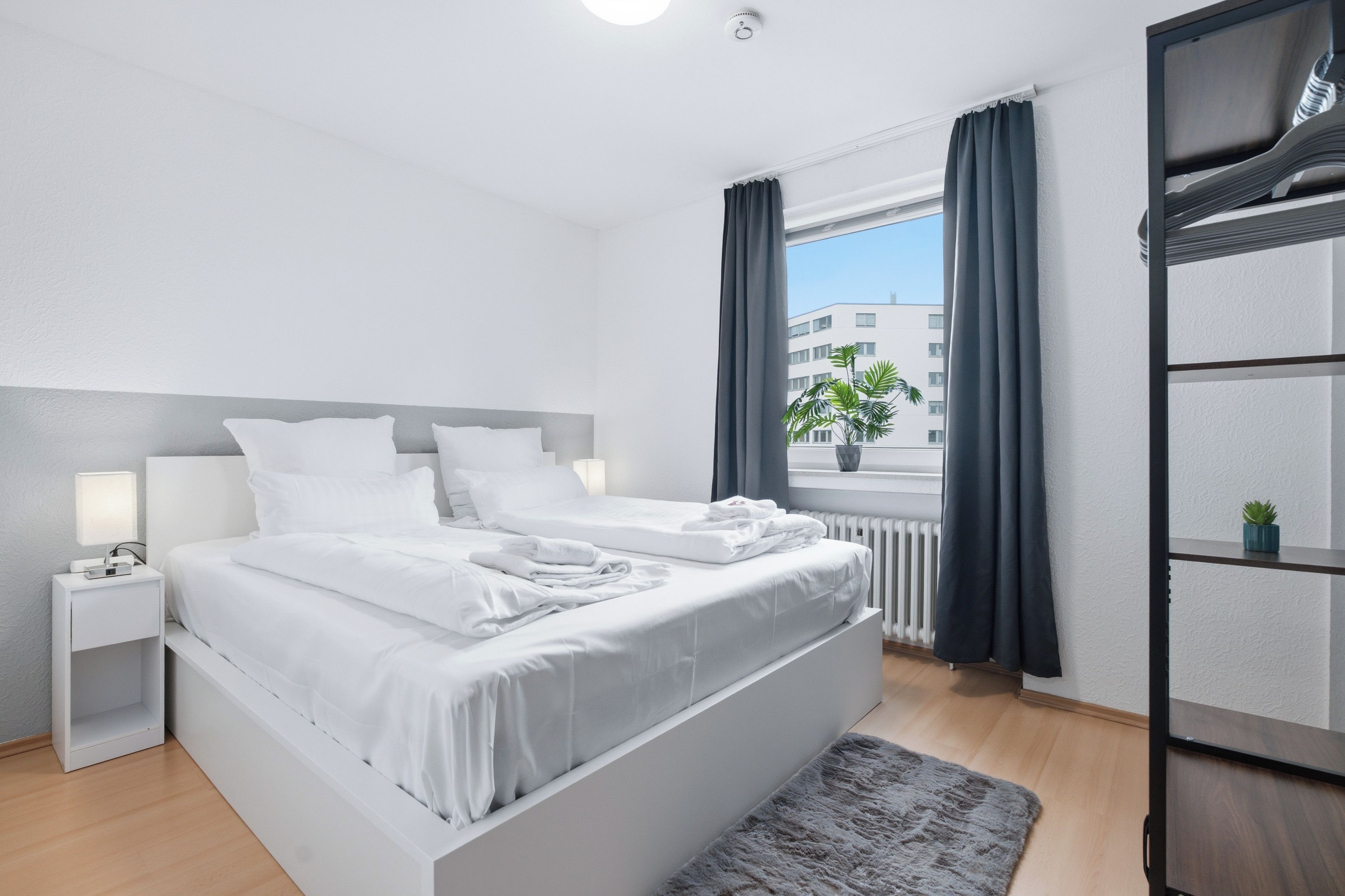 Ein modernes Schlafzimmer mit einem großen Bett, Nachttischen, einem Heizkörper und einem Fenster mit Vorhängen.