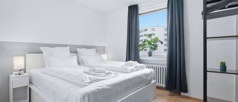 A modern bedroom with a large bed, bedside tables, a radiator, and a window with curtains.