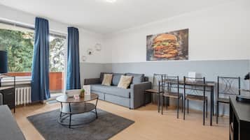 A modern living room with a grey sofa, a dining table with chairs, a coffee table, and a large painting of a burger.