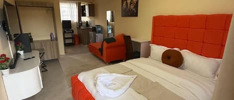Een hotelkamer met een groot bed, een bureau, een stoel, een televisie en een kitchenette op de achtergrond.