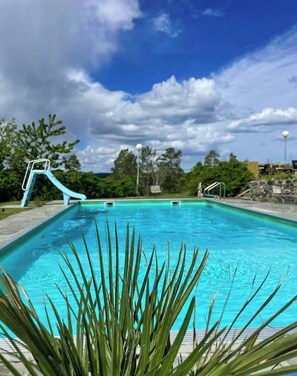 A swimming pool with a slide, surrounded by greenery and a clear sky. - Modern cabin with jacuzzi in Risør (Søndeled)