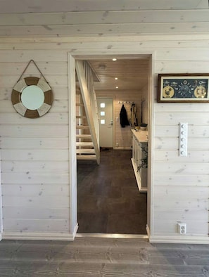 A hallway with a wooden staircase leading to a room with a white wall, a framed picture, and a light switch. - Modern cabin with jacuzzi in Risør (Søndeled)