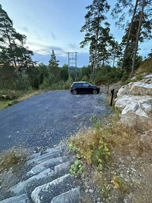 A gravel road with a car parked on the side, surrounded by trees and rocky terrain. - Modern cabin with jacuzzi in Risør (Søndeled)