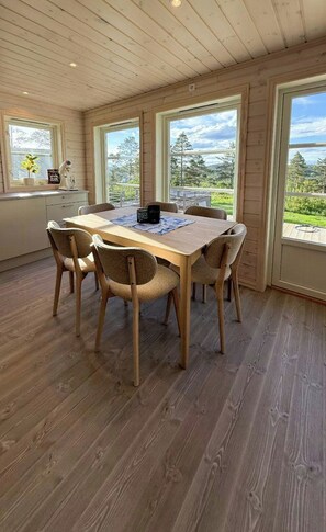 A dining area with a wooden table and chairs, large windows, and a view of the outdoors. - Modern cabin with jacuzzi in Risør (Søndeled)